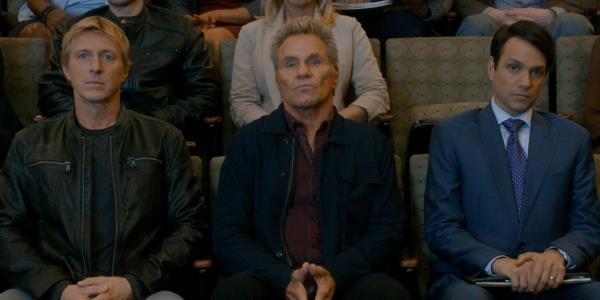 Johnny Lawrence, John Kreese, and Daniel LaRusso sitting beside each other in a row in Cobra Kai.